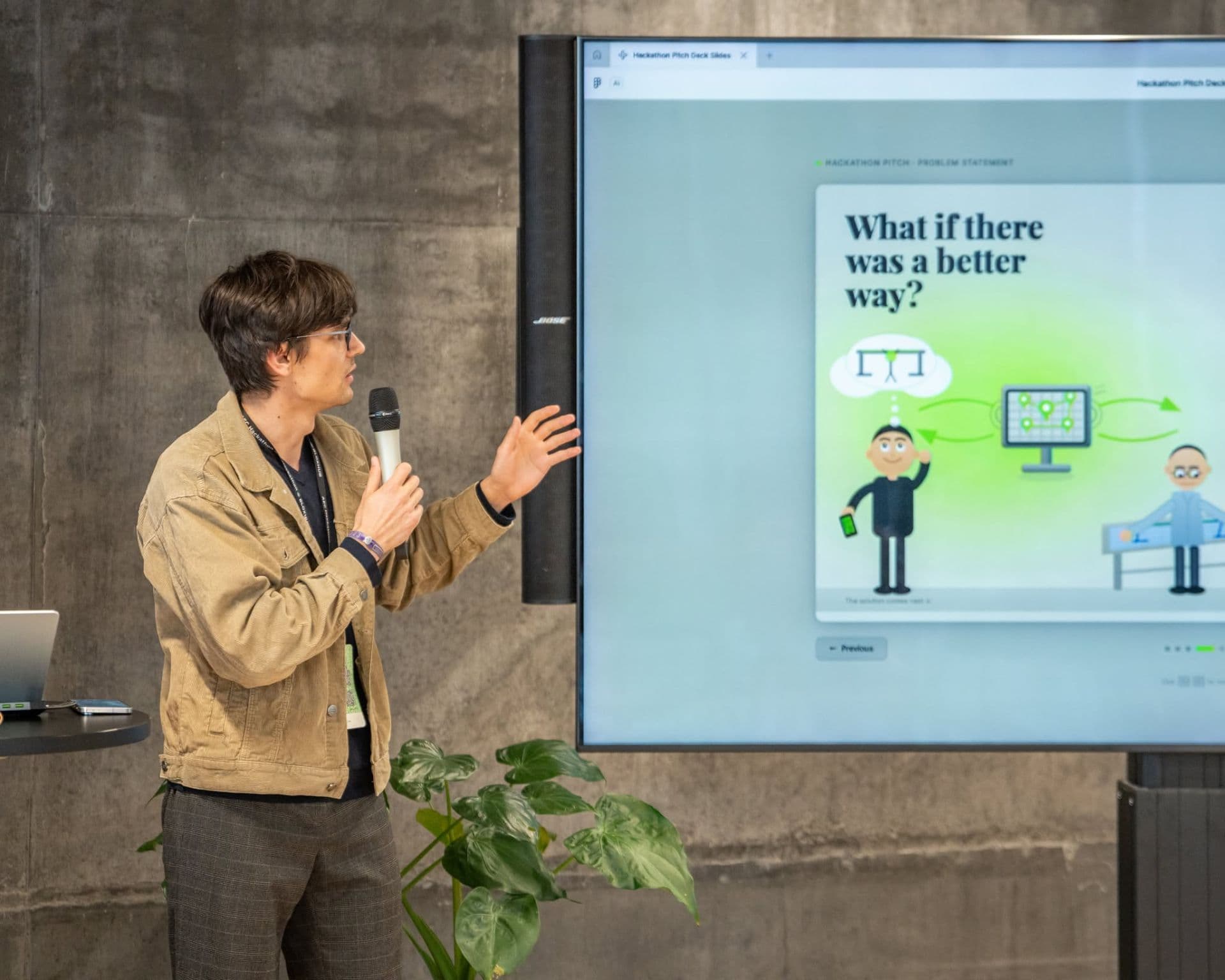 Delivering the Klaudiush pitch at AEC Hackathon Copenhagen — problem-statement slide ('What if there was a better way?') projected on a screen behind the presenter